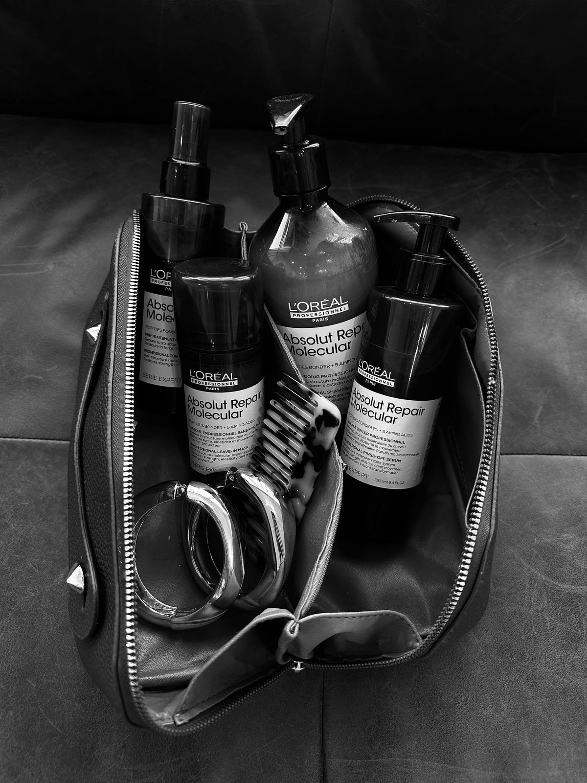 A black and white photograph of a small zipped bag containing hair care products, including bottles of L at Eve Salon, Saint Louis MO