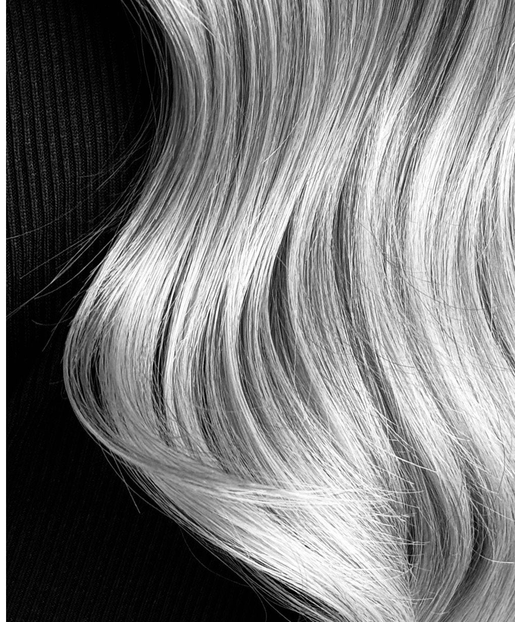 Close-up of silver-blonde hair with soft, flowing waves against a dark background. at Eve Salon, Saint Louis MO